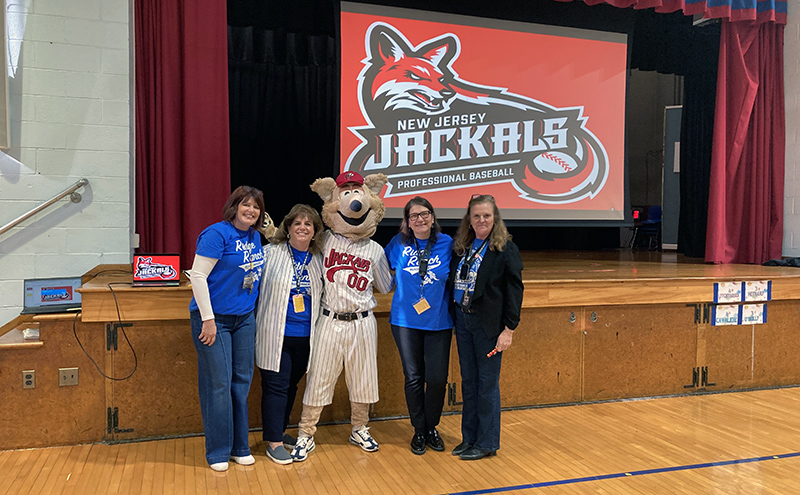 Jack the Jackal mascot with school admin team in the in front of a stage