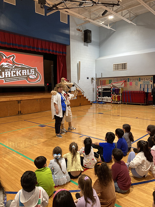 Jack the Jackal talking with students sitting on the gym floor