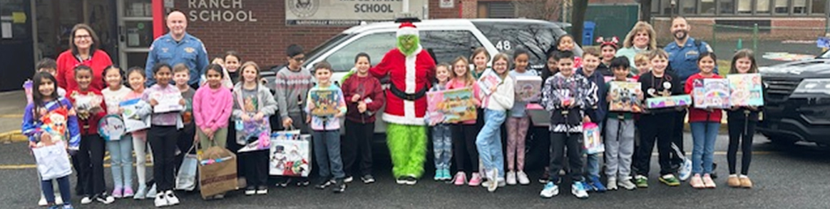 Group of students outside school building with teachers and Grinch from Dr. Seuss