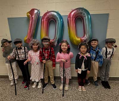 Student dressed up as elders under a sign that reads 100