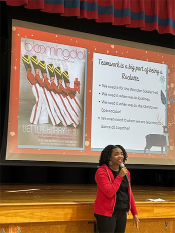 Member of the Rockettes during another part of her presentation with large presentation screen behind her