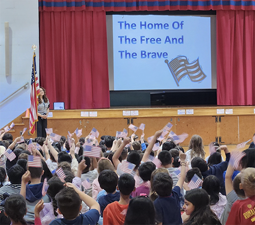 Students waving flags as students sing on stage